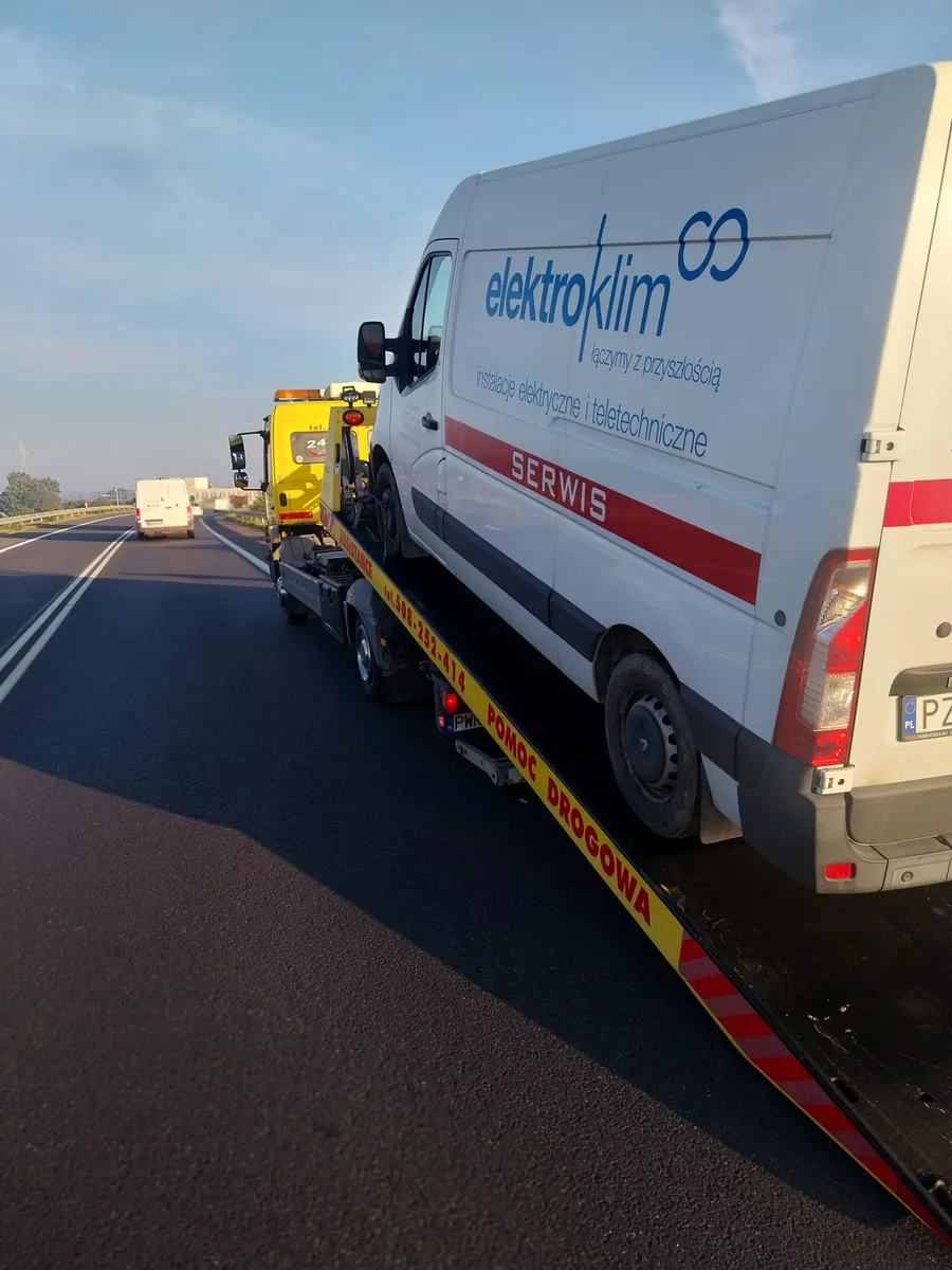 Laweta transportująca białego busa Renault Master z naklejką firmową